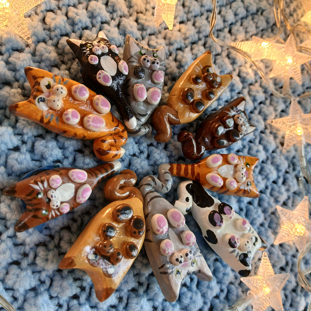 Collection of clay cat-shaped magnets, on light blue textured background, with decorative star lights.