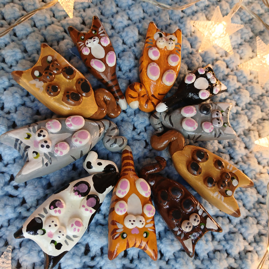 Collection of clay cat-shaped magnets, on light blue textured background, with decorative star lights.