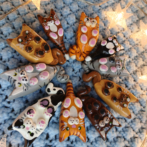 Collection of clay cat-shaped magnets, on light blue textured background, with decorative star lights.