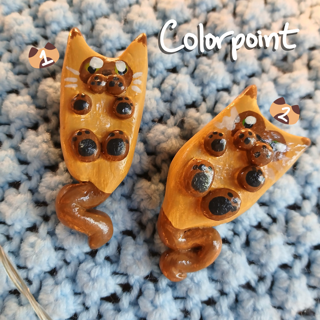 Two clay colorpoint cat-shaped magnets, on light blue textured background, with decorative star lights.