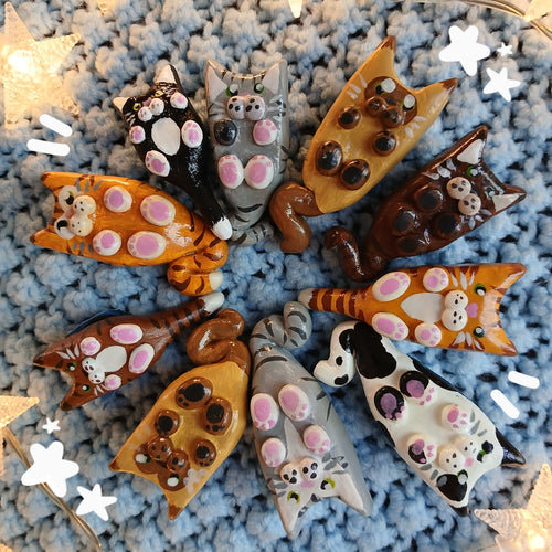 Collection of clay cat-shaped magnets, on light blue textured background, with decorative star lights.